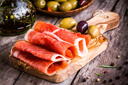 Thin Slices of Prosciutto with Mixed Olives on Wooden Cutting Board